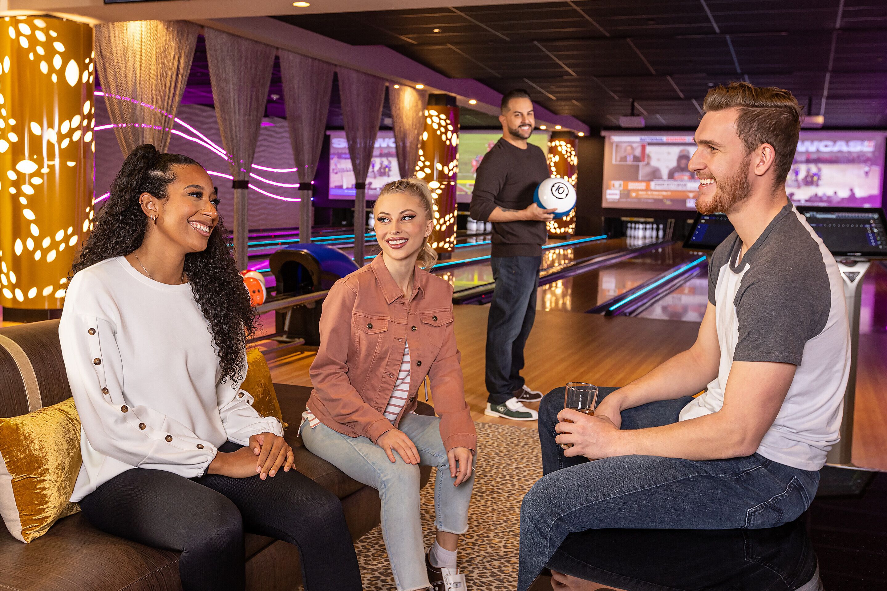 Eine Kegelbahn mit Sitzgelegenheit, einer Bowlingbahn und einem Bildschirm, der ein Spiel zeigt.