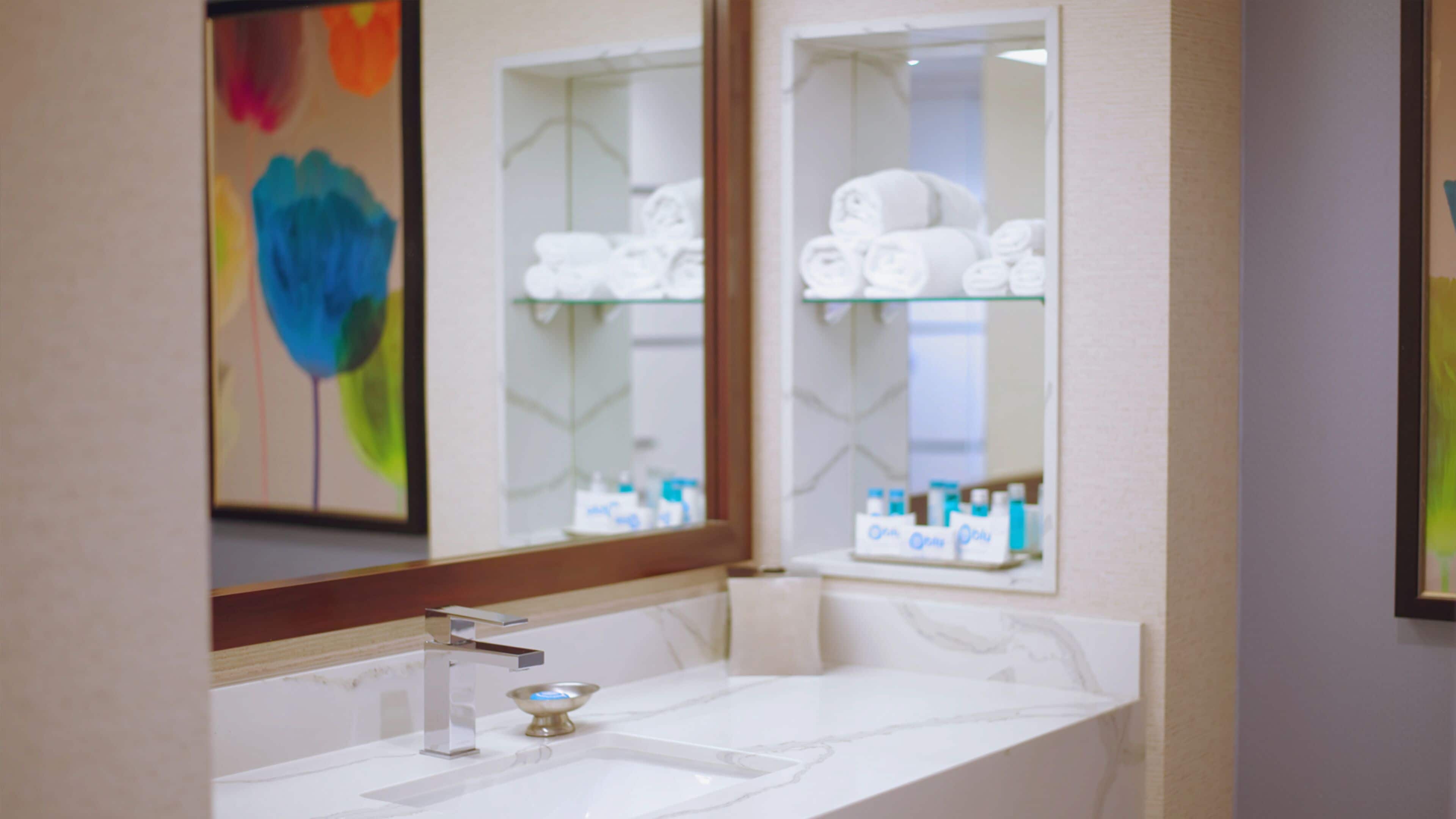 A bathroom with a white sink, a mirror, and shelves with toiletries.