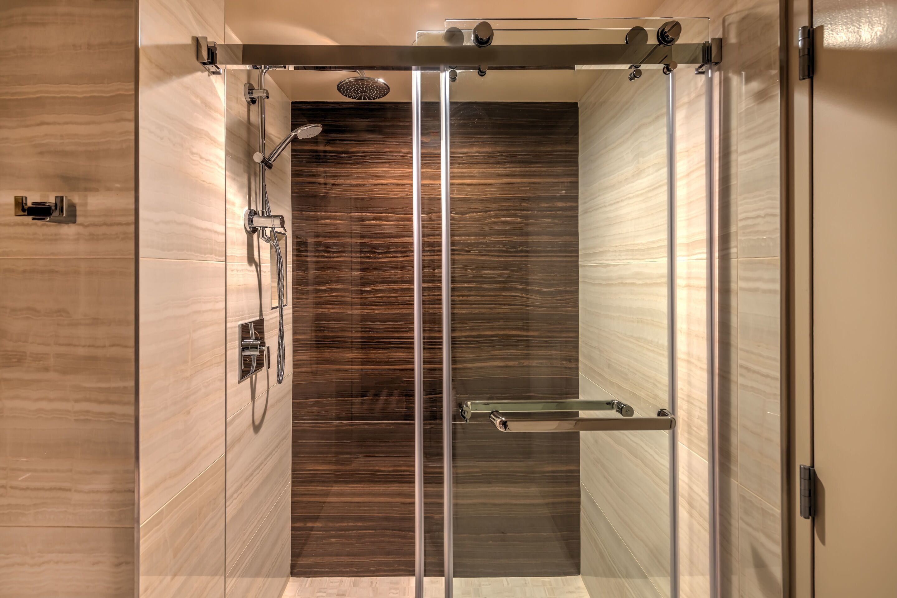 Een moderne douche met een glazen deur, een handdouche en een stortdouche.