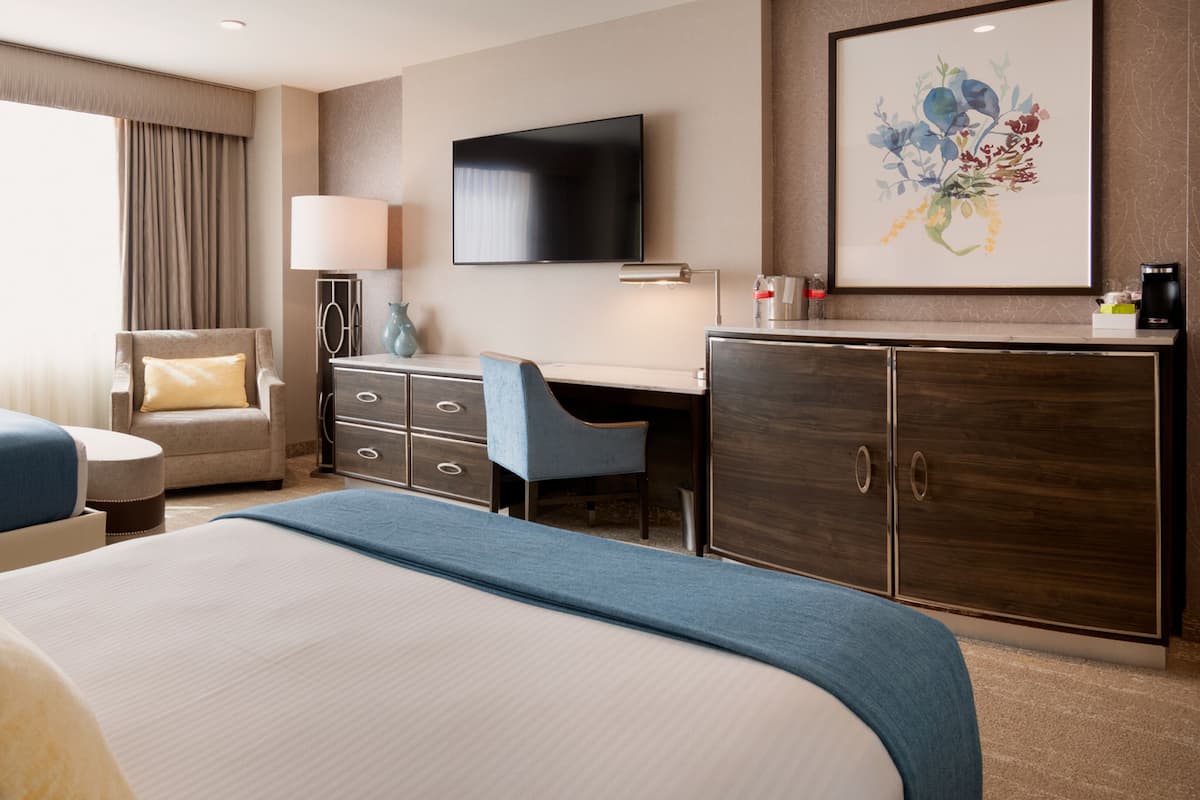 Ein Hotelzimmer mit einem großen Bett, einem Schreibtisch, einem Stuhl, einem Fernseher und einem Schrank.