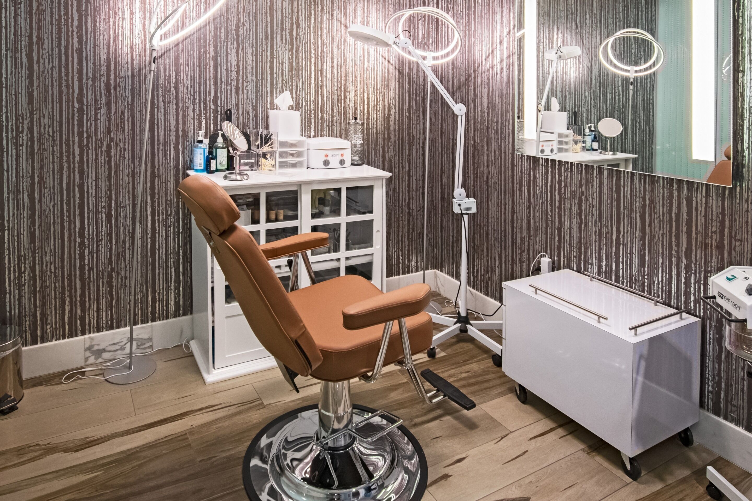 A modern salon with a leather chair, a white vanity, and a mirror with lights.