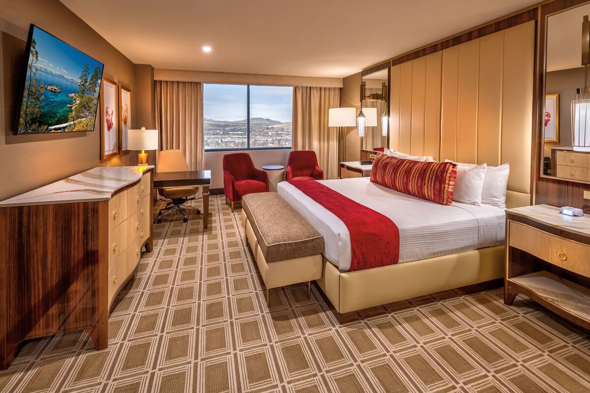 Ein Hotelzimmer mit einem großen Bett, einem Schreibtisch mit Stuhl, einem kleinen Tisch und Blick auf die Stadt.