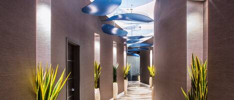 A modern hallway with a patterned floor, potted plants, and blue ceiling lights.
