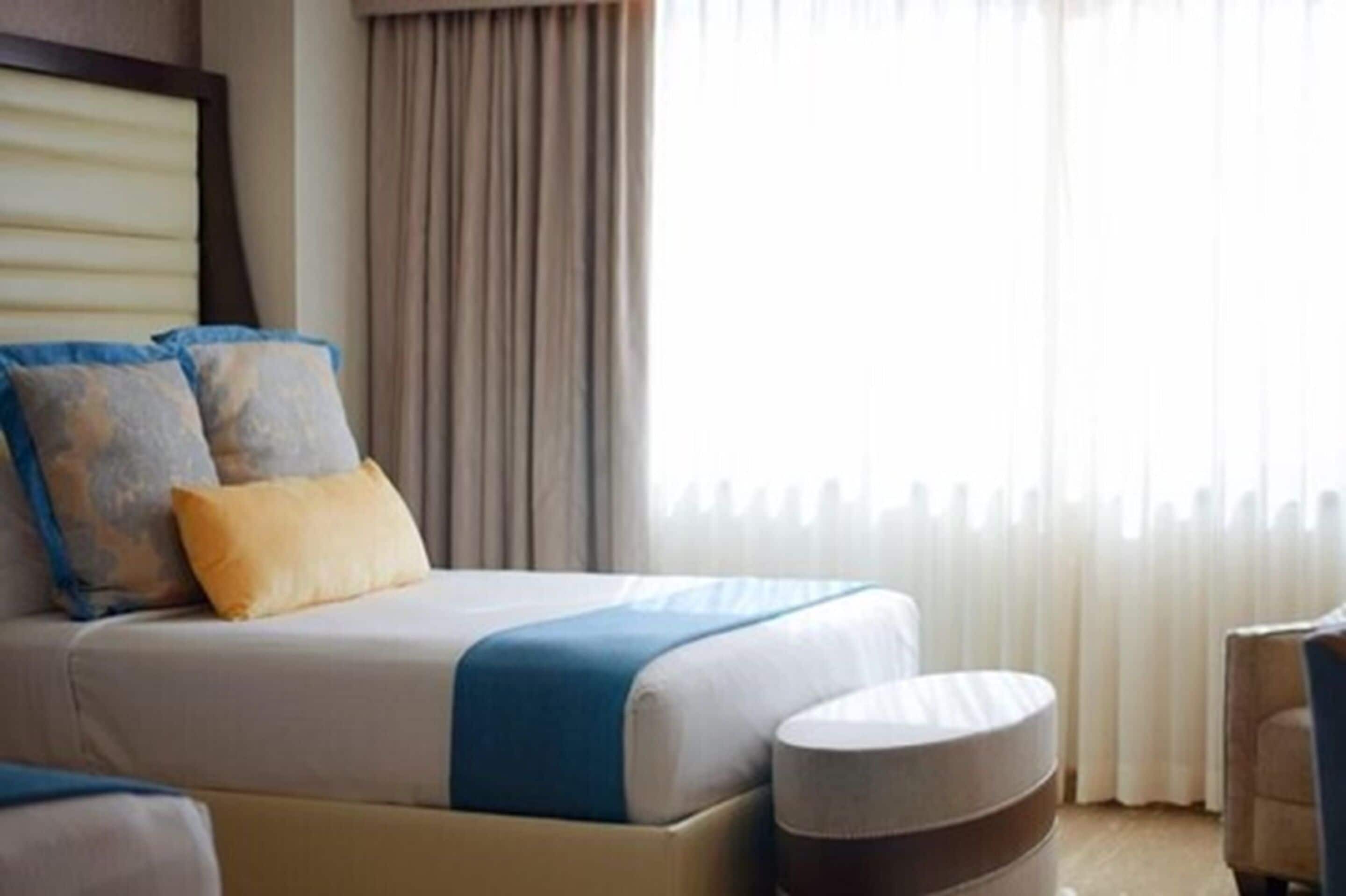 A hotel room with a bed, a bedside table, and a window with curtains.