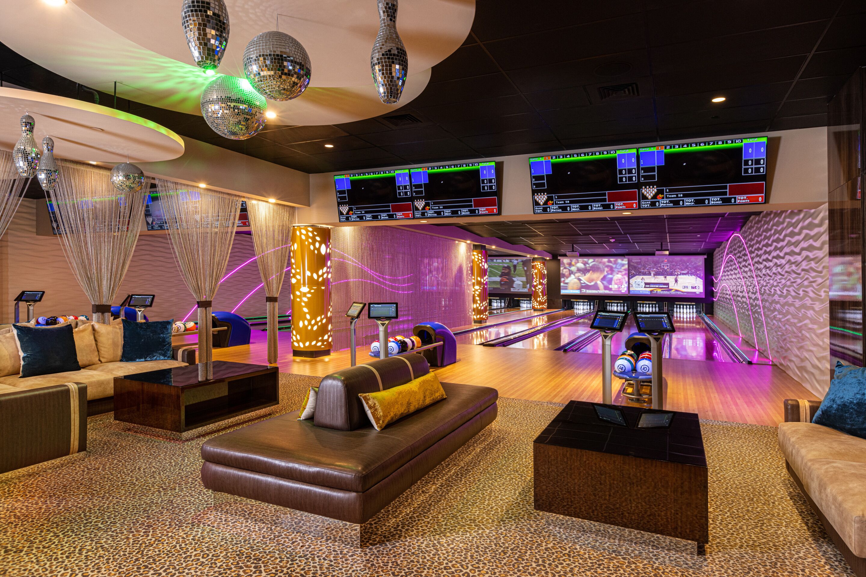 A bowling alley with multiple lanes, a seating area with couches and a coffee table, and overhead scoreboards.