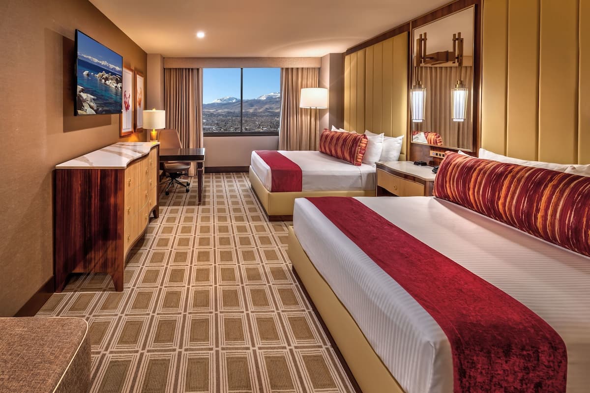Ein Hotelzimmer mit zwei Betten, einem Schreibtisch, einem Stuhl und Bergblick durch das Fenster.