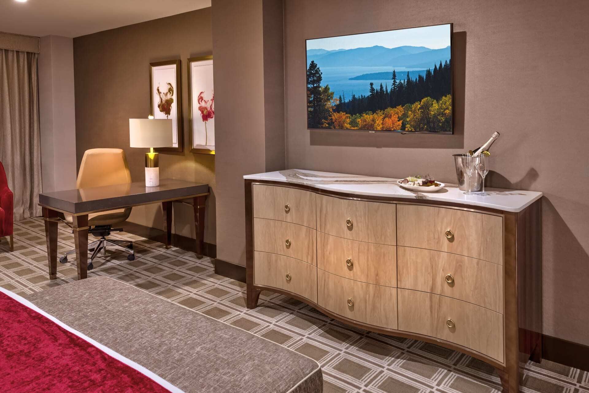 A hotel room with a dining table, a sofa, a cabinet with a mirror, and a large window with a scenic view.