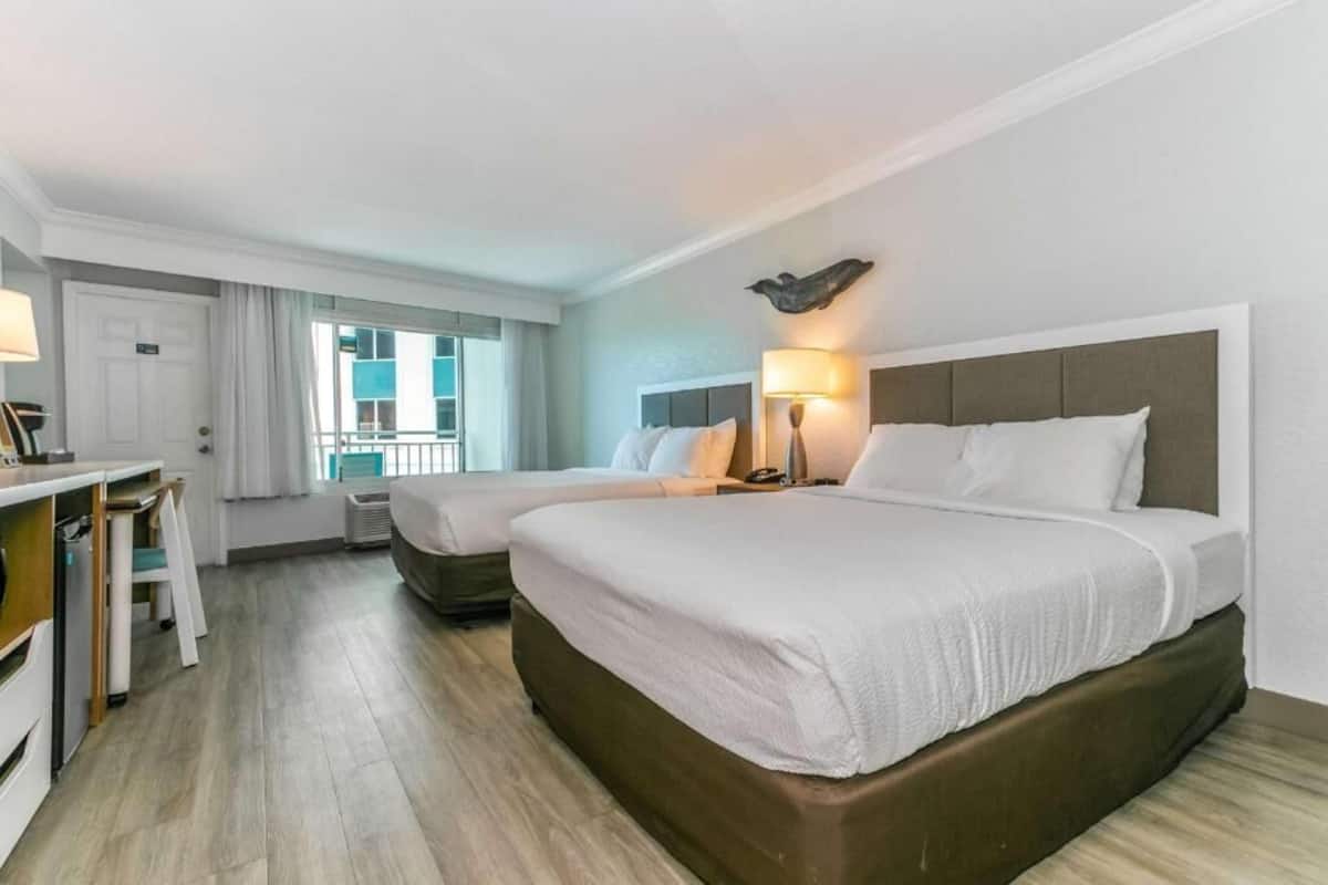 Une chambre d’hôtel avec deux lits, un bureau et une fenêtre avec des rideaux.