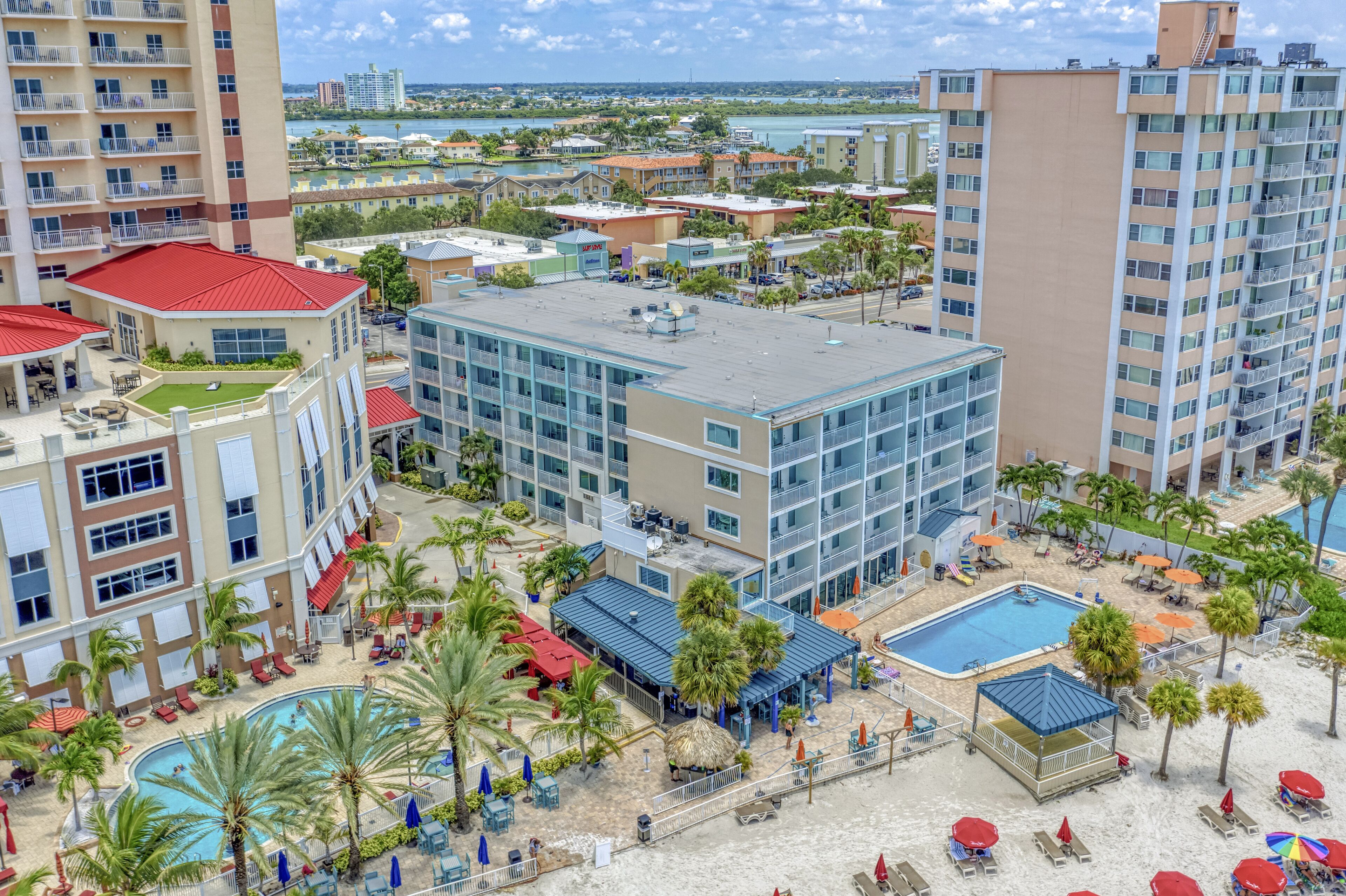 A hotel with multiple buildings, a swimming pool, and a beach area with umbrellas and lounge chairs.