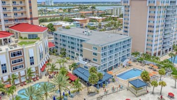 A hotel with multiple buildings, a swimming pool, and a beach area with umbrellas and lounge chairs.