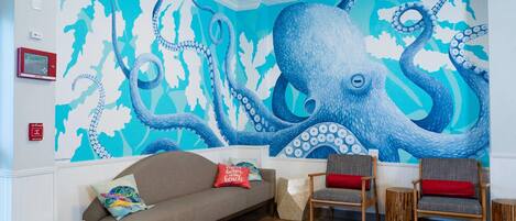 Quarto com um grande mural de polvo, um sofá, duas cadeiras e uma pequena mesa de madeira.