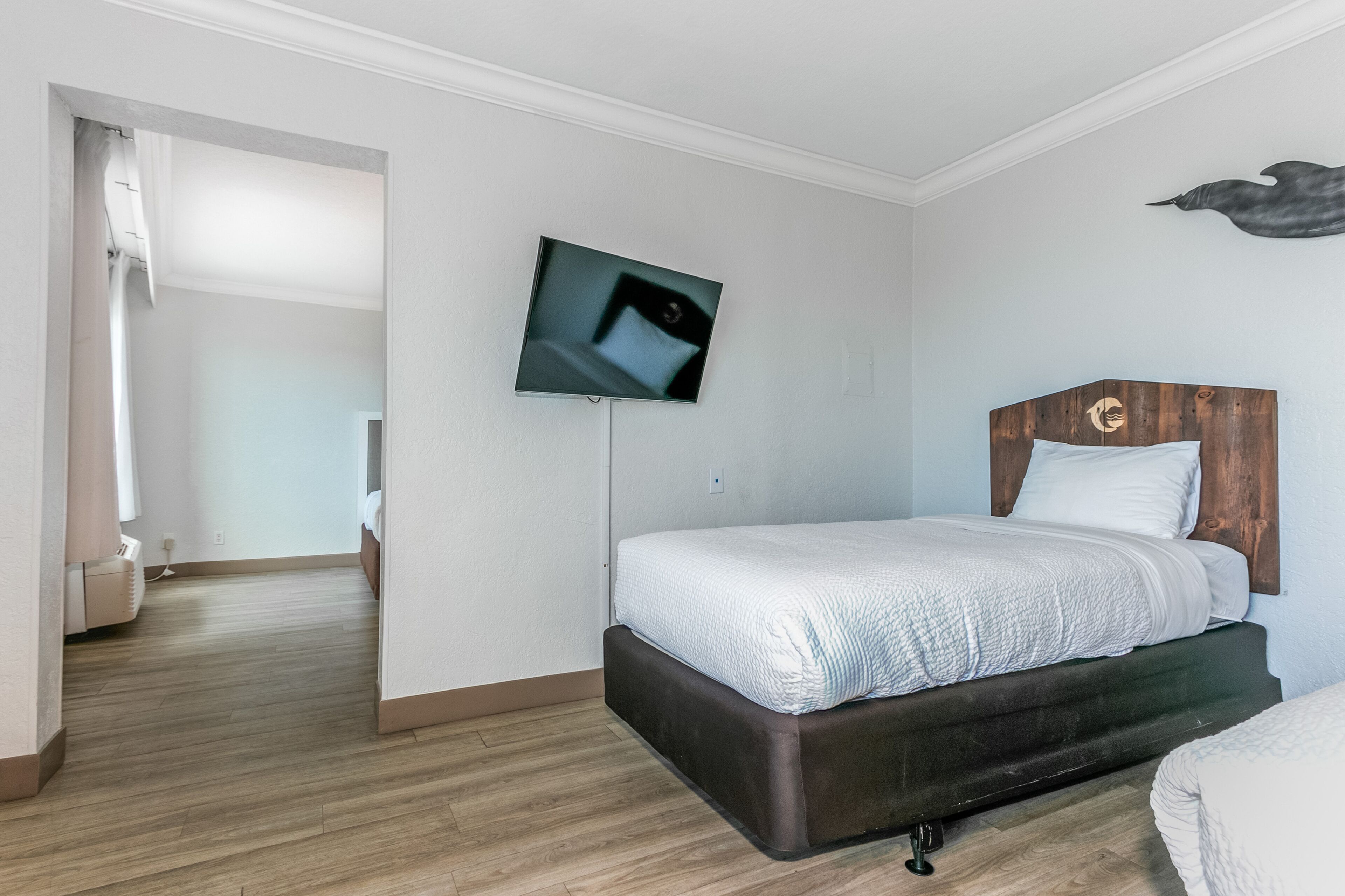 A bedroom with a bed, a mounted TV, a wooden headboard, and a shower area.