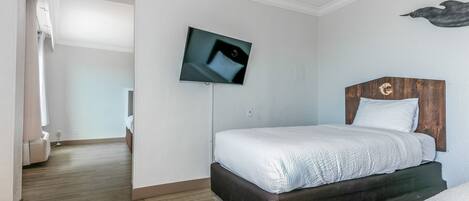 A bedroom with a bed, a mounted TV, a wooden headboard, and a shower area.
