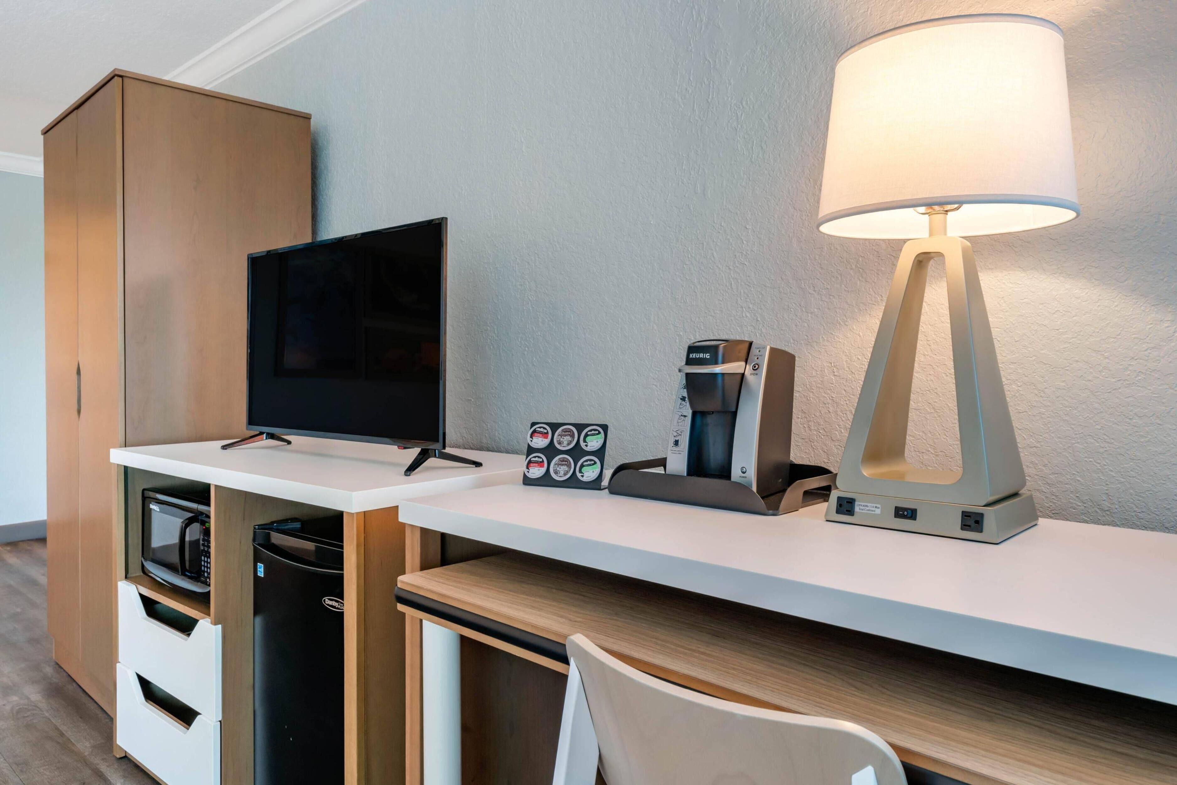 A hotel room with a flat-screen TV, a coffee machine, a lamp, a minibar, and a wooden wardrobe.