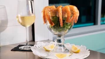 A glass bowl with cooked shrimp on a bed of lettuce, accompanied by a glass of white wine and lemon slices on a white doily.