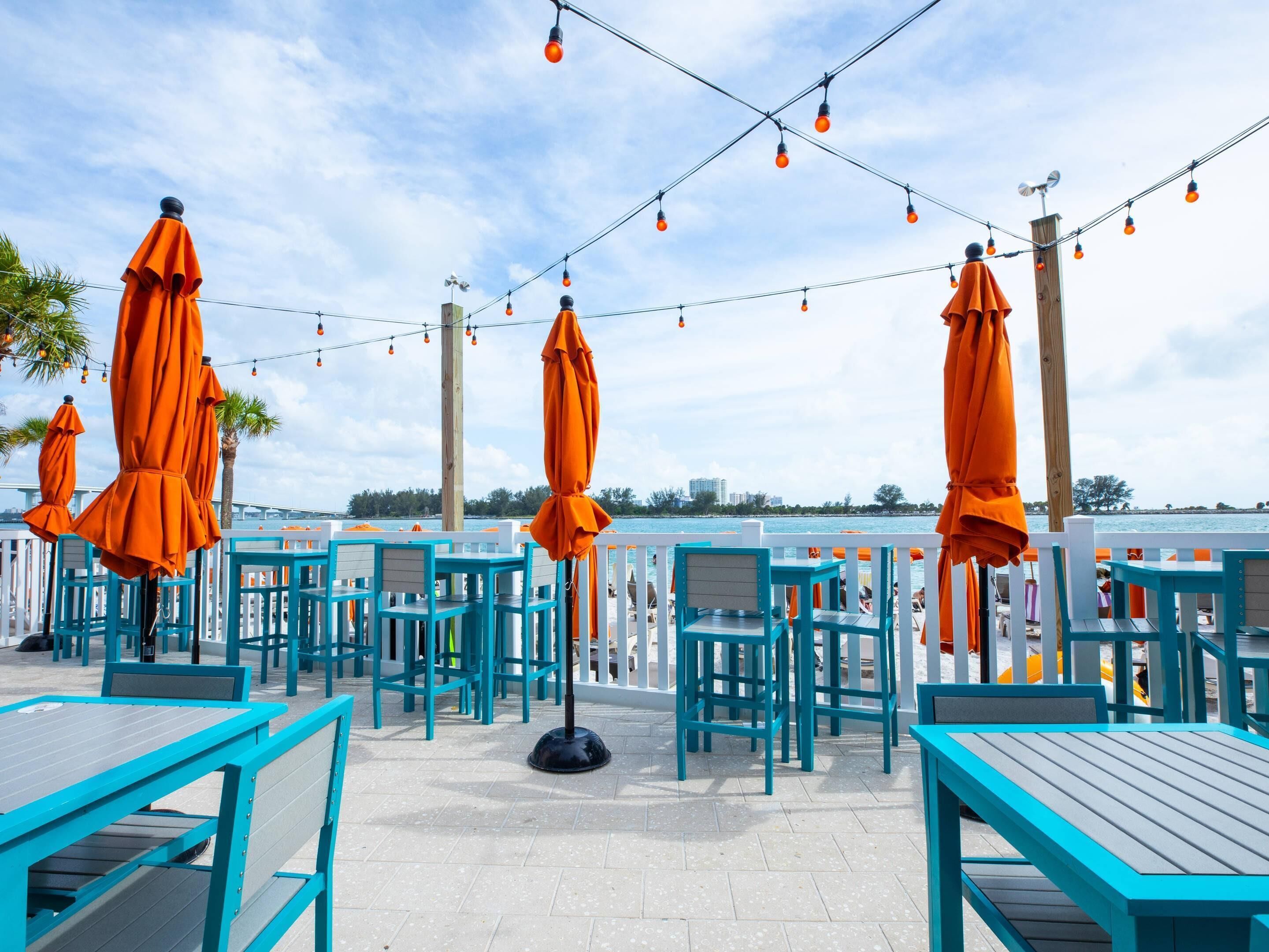 Outdoor seating with tables and chairs, string lights overhead, and a view of the water.