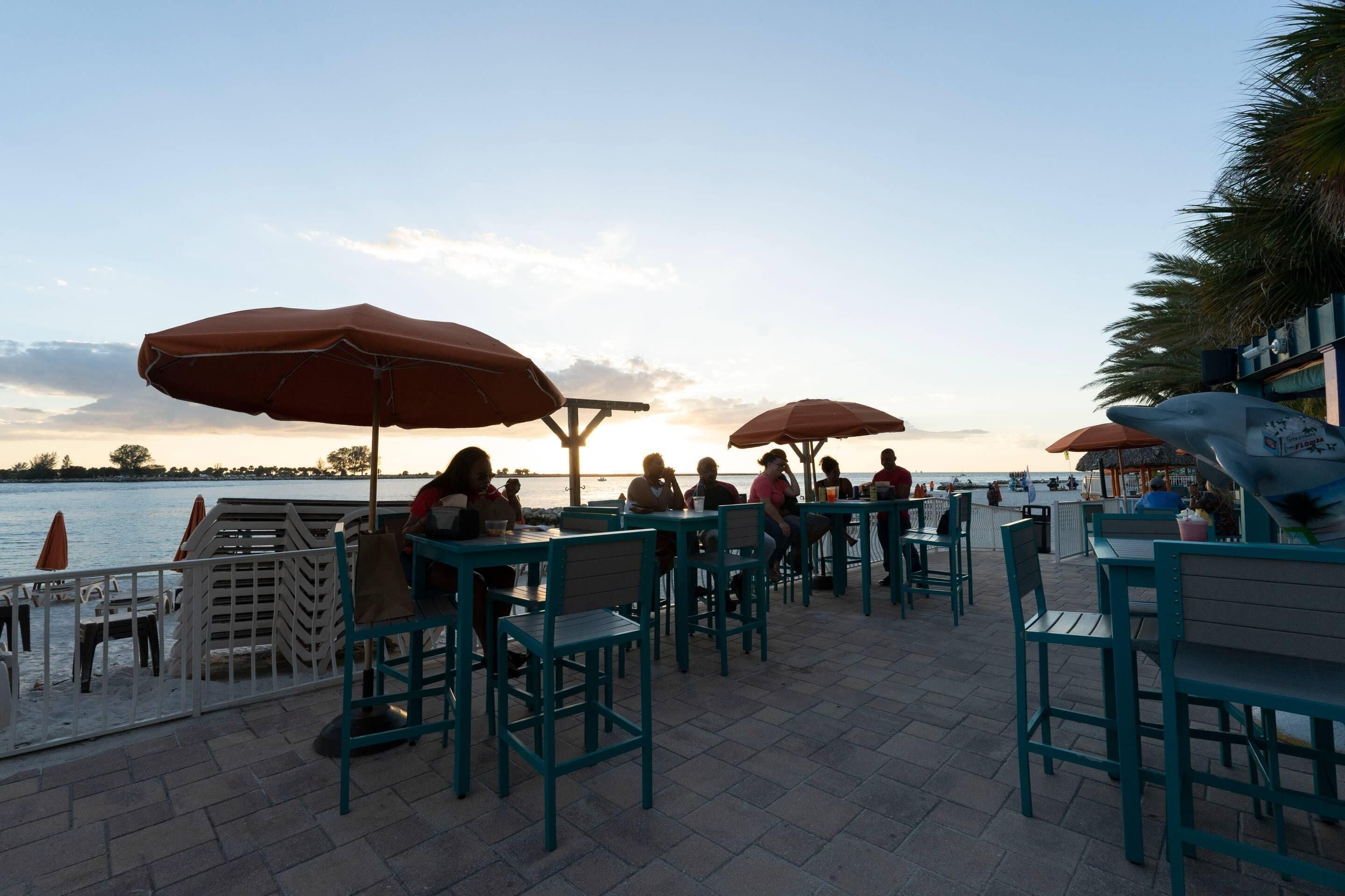 An outdoor seating area with tables and chairs, umbrellas, and a view of the water.