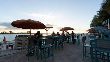 An outdoor seating area with tables and chairs, umbrellas, and a view of the water.