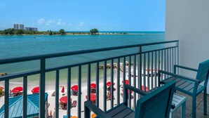 Un balcon avec vue sur une plage et l’océan, équipé de mobilier d’extérieur et de parasols.