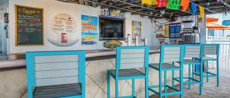Een bar met turquoise stoelen, een toonbank en verschillende posters met aanbiedingen en drankjes.