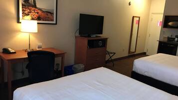 Et hotelværelse med to senge, et skrivebord med telefon, et fjernsyn på et træskab og et billede i ramme på væggen.