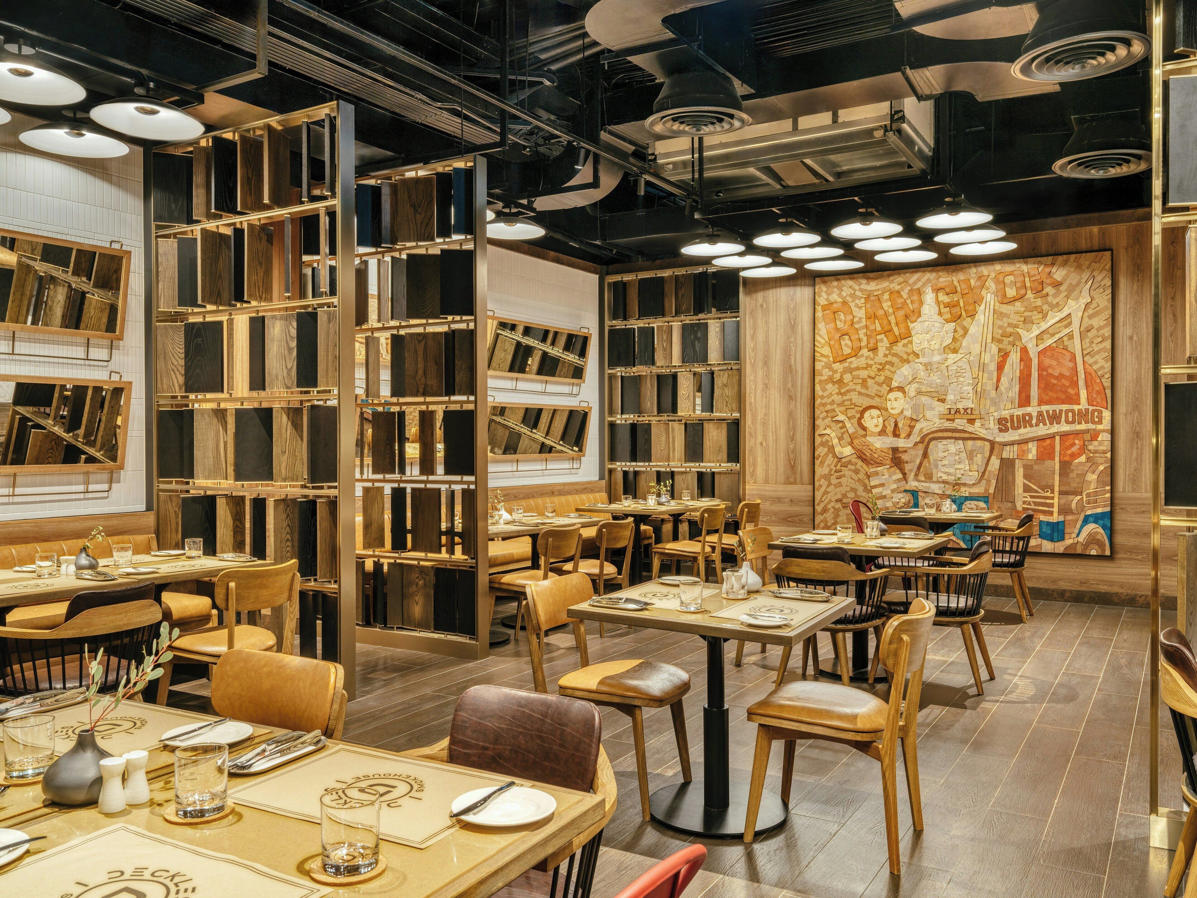 A restaurant interior with multiple dining tables and chairs, wooden paneling on the walls, and a mural depicting a taxi and the word 'SURAWONG'.
