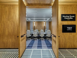 A meeting room with a checkered carpet, a table with chairs, and a sign indicating 'Meeting Room Gunsudha'.
