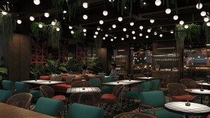 Un interior de restaurante con plantas colgantes, mesas redondas y sillas.