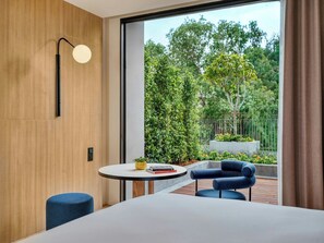 Habitación de hotel moderna con un ventanal grande, una mesa redonda con libros, una silla azul y una cama.
