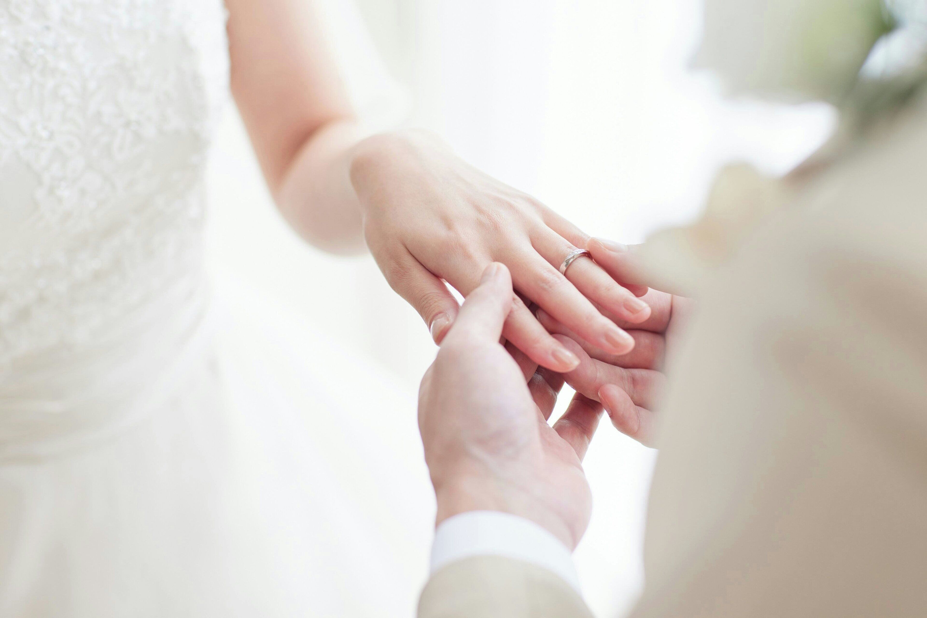 A close-up of a bride and groom holding hands, focusing on their hands and rings.