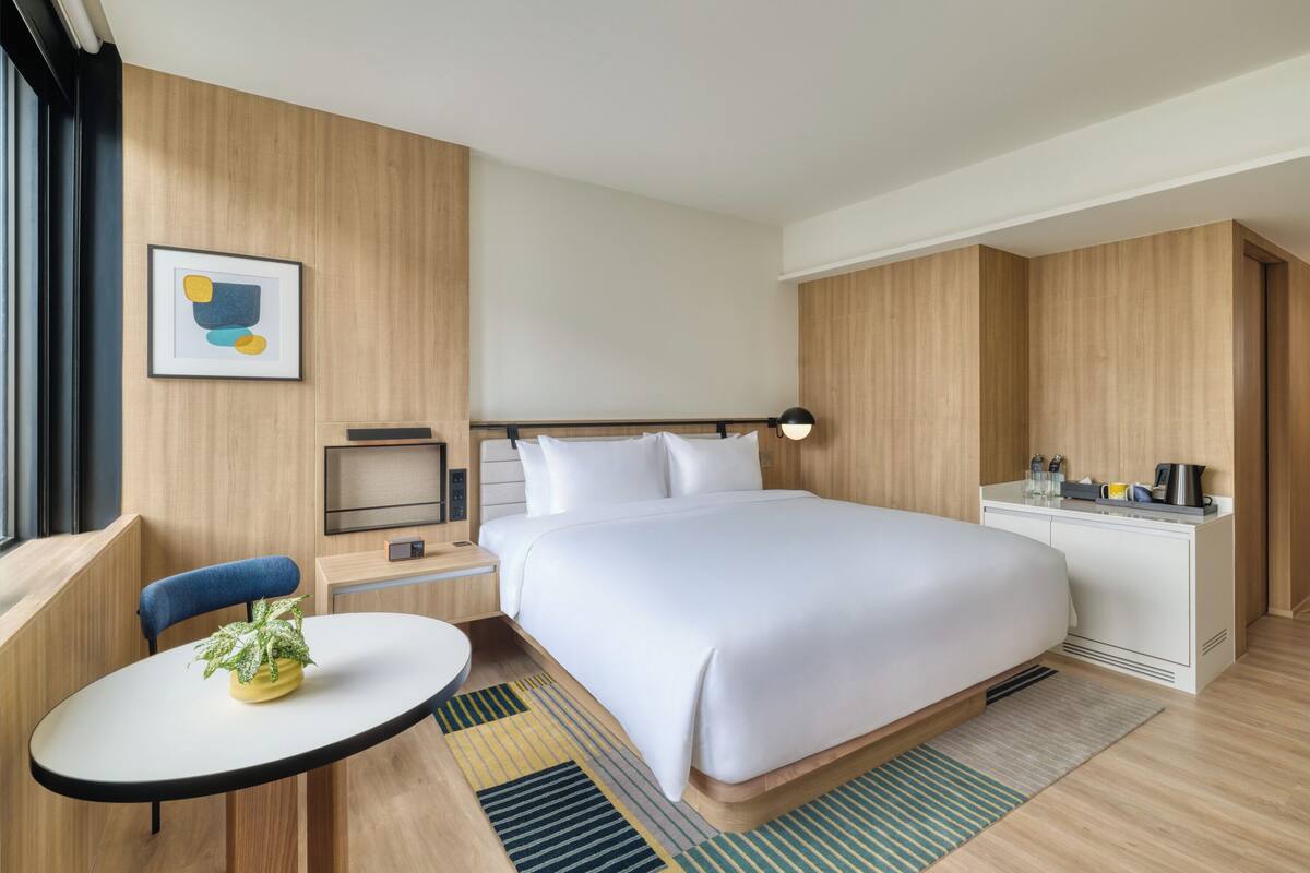 Une chambre d’hôtel moderne avec un grand lit, un petit bureau, une chaise, une table de chevet et une fenêtre.