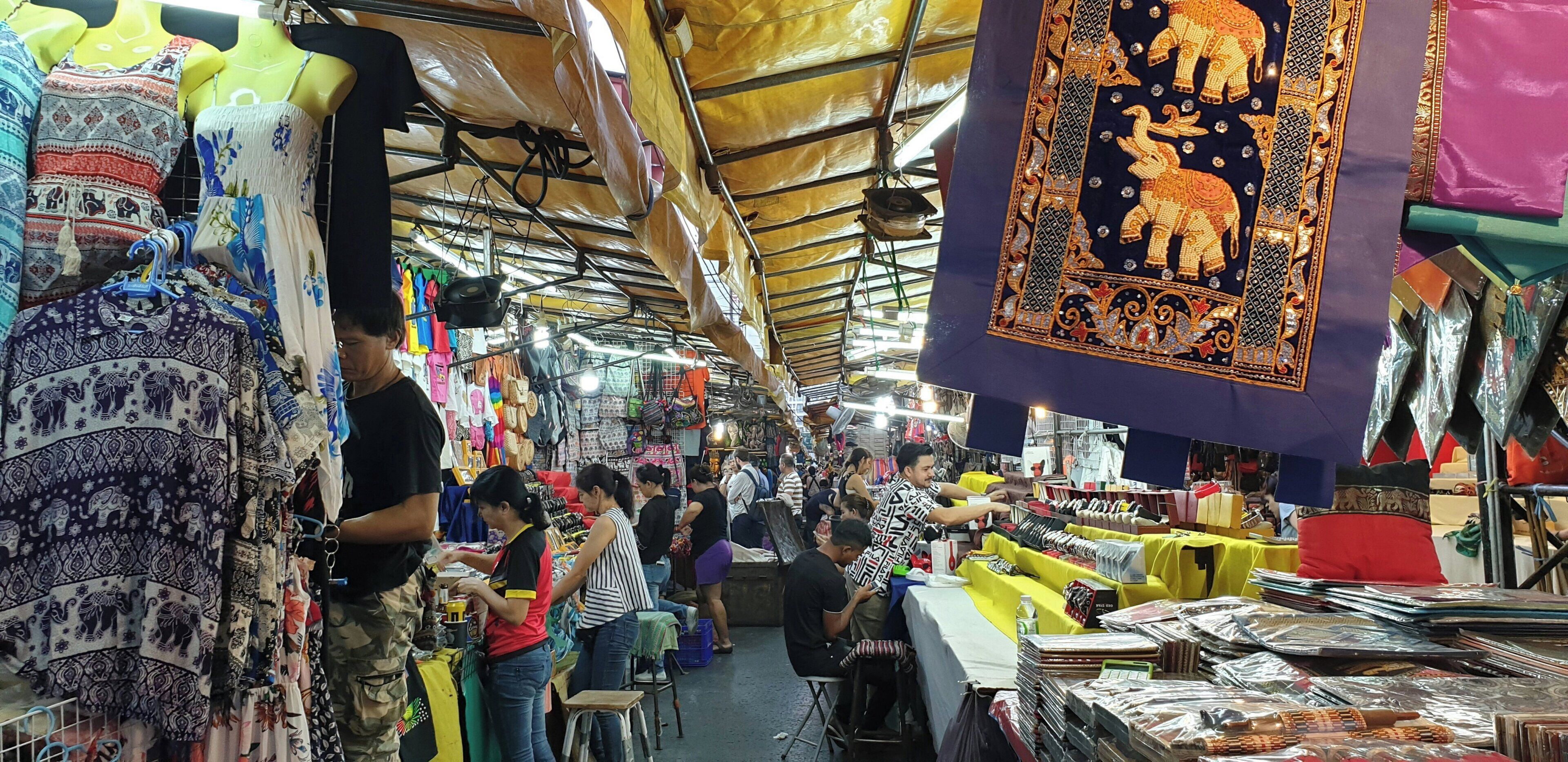 A bustling indoor market with various stalls selling textiles and clothing.
