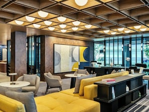 Un vestíbulo moderno con un diseño geométrico en el techo, un cuadro abstracto de gran tamaño y una zona de estar con un sofá y sillones amarillos.