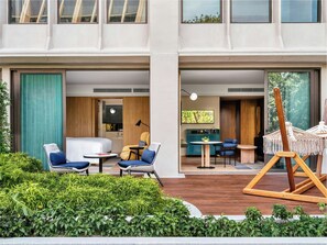 A modern hotel room with a bed, seating area, and a view of the greenery outside.