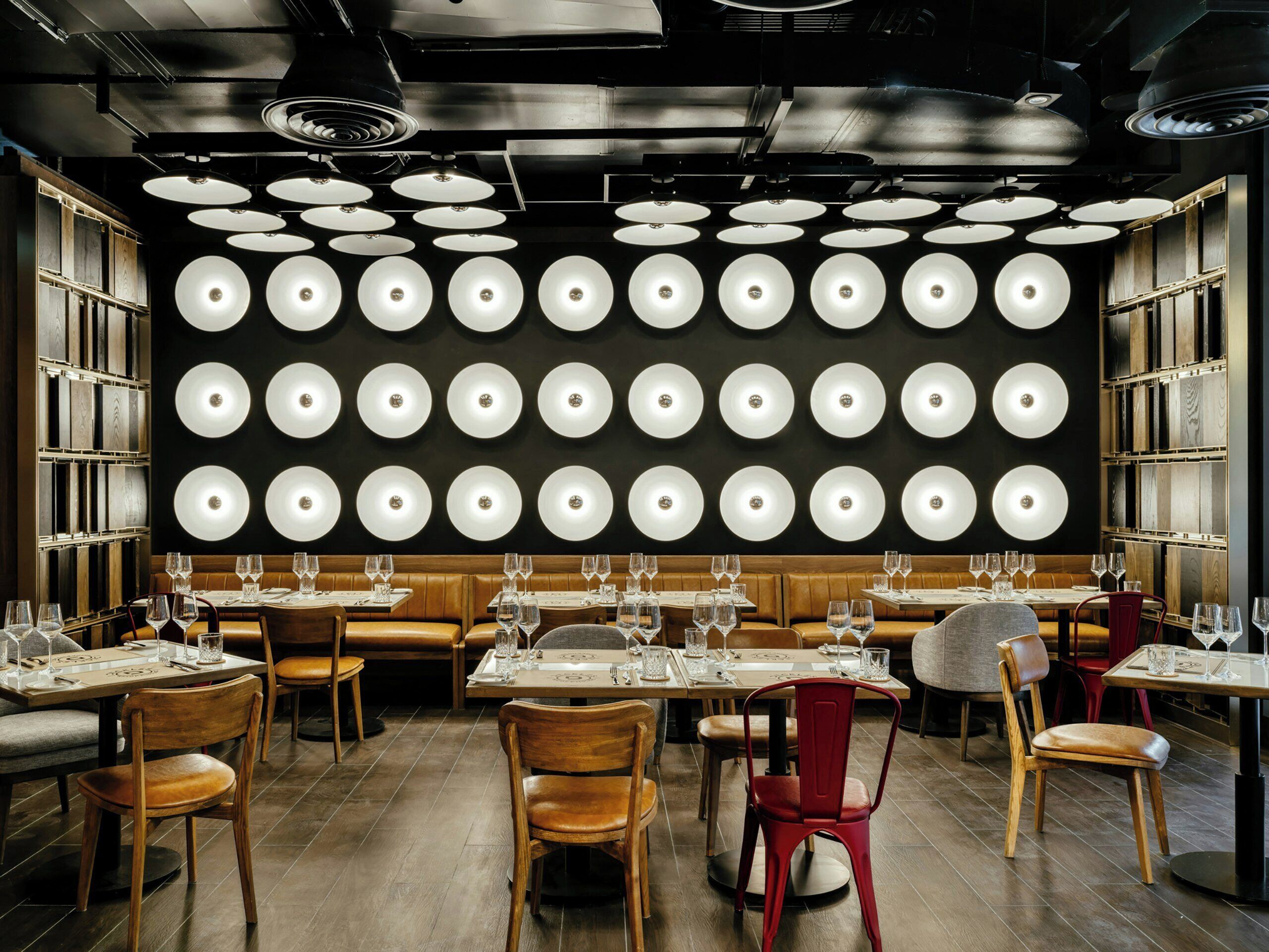 A restaurant interior with multiple tables, chairs, and a wall of circular light fixtures.