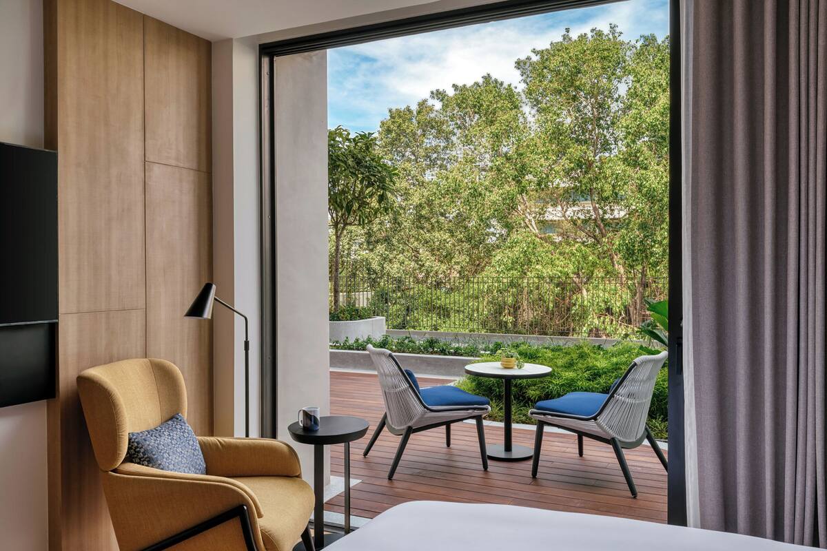 Une chambre d’hôtel avec une grande fenêtre, un lit, une chaise, une petite table et un téléviseur fixé au mur.