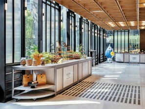 A modern interior with a long counter displaying food and drinks, large windows, and a clean, polished floor.