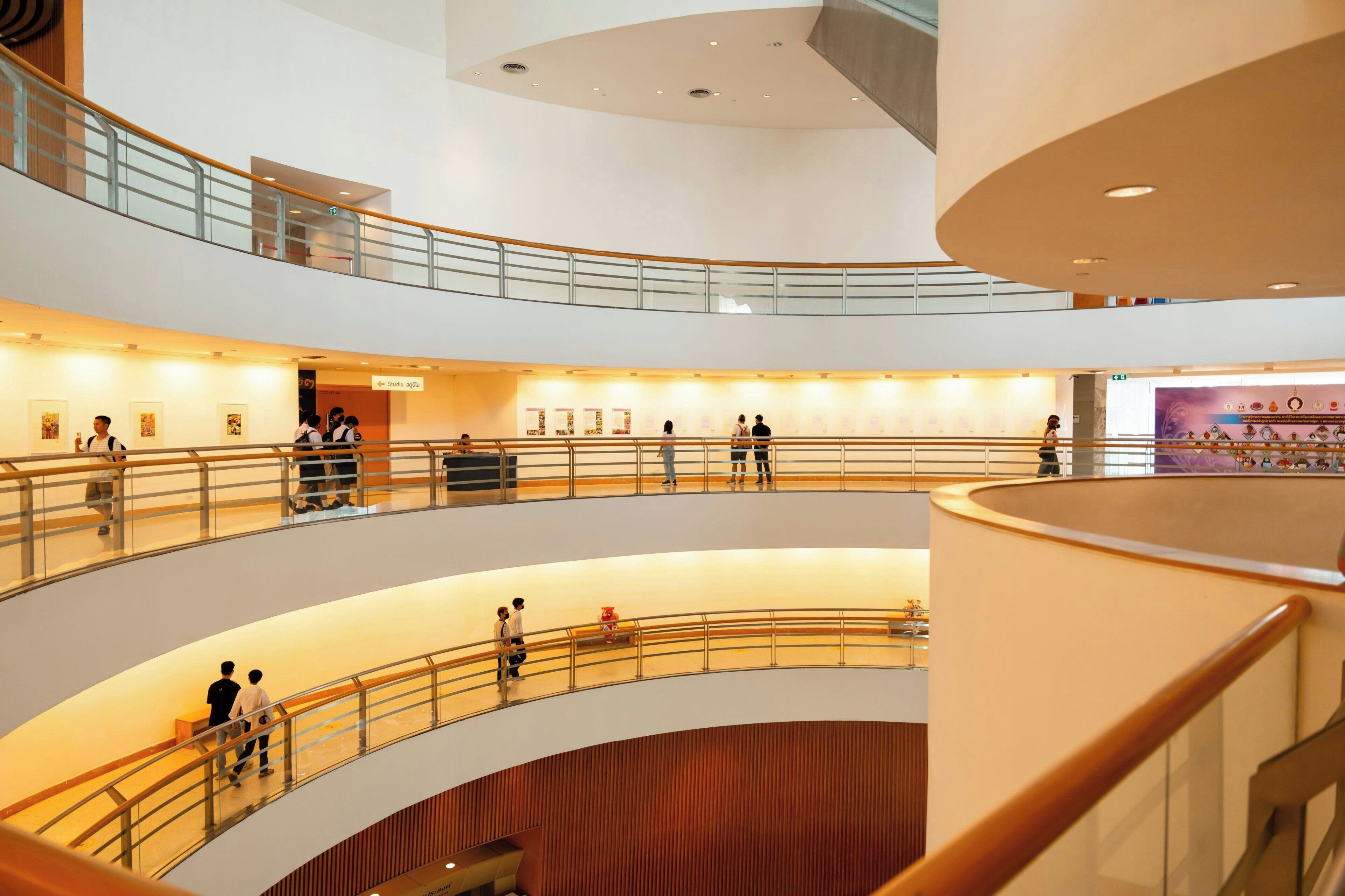 A multi-level atrium with glass railings, artwork on the walls, and people walking.