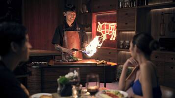 A restaurant interior with wooden furniture, a neon sign, and a chef performing a cooking demonstration.