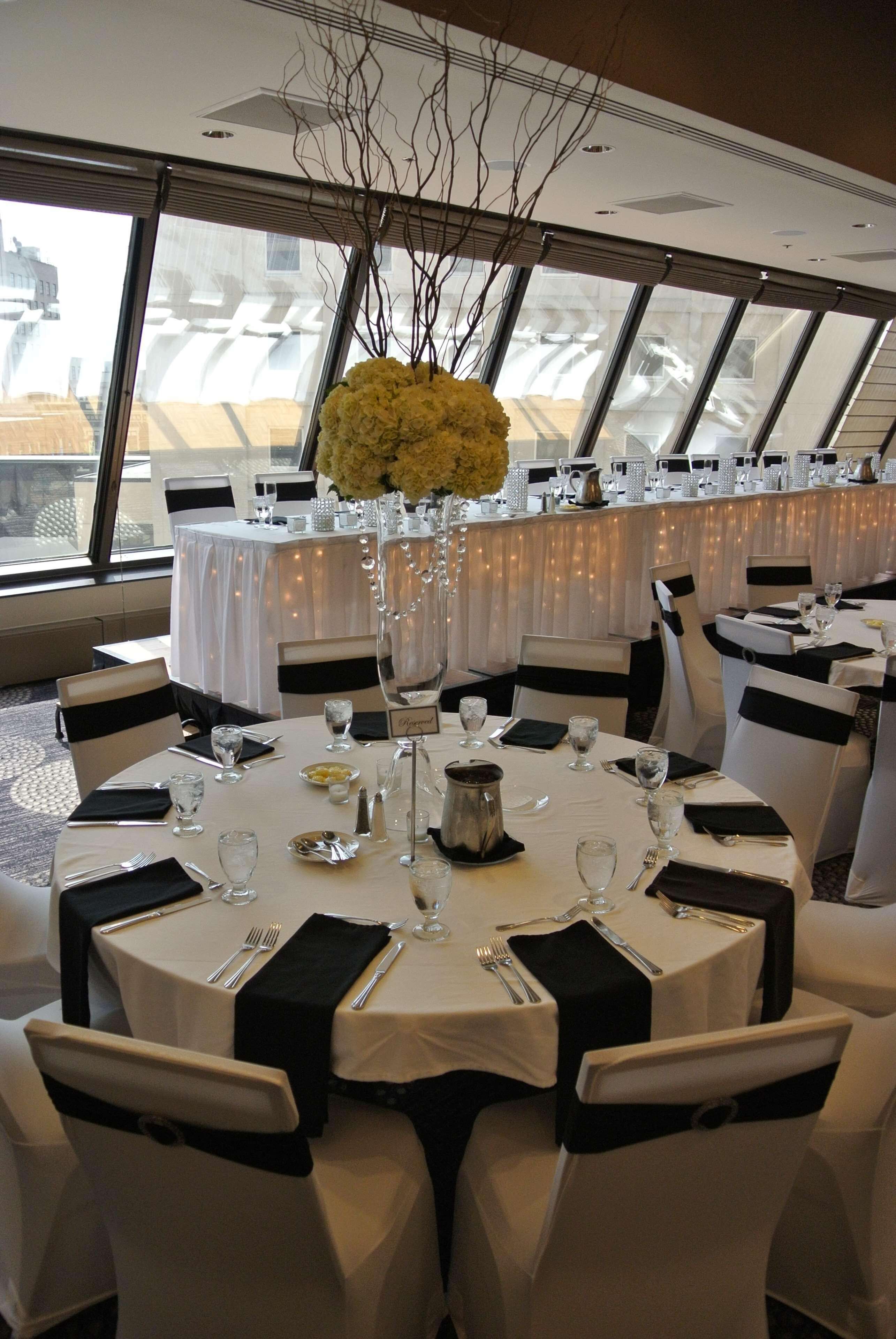 Un salón de banquetes con mesas redondas, manteles blancos y cintas negras en las sillas.