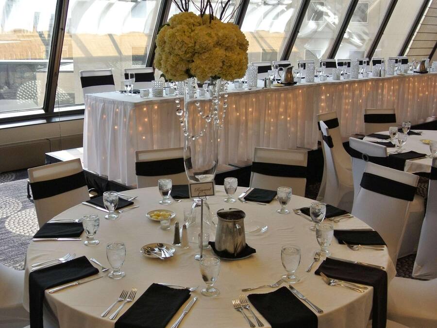 Un salón de banquetes con mesas redondas, manteles blancos y cintas negras en las sillas.