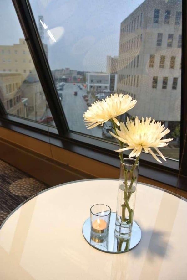 Uma mesa com um vaso de flores e uma vela, vista através de uma janela com vista para uma rua da cidade.