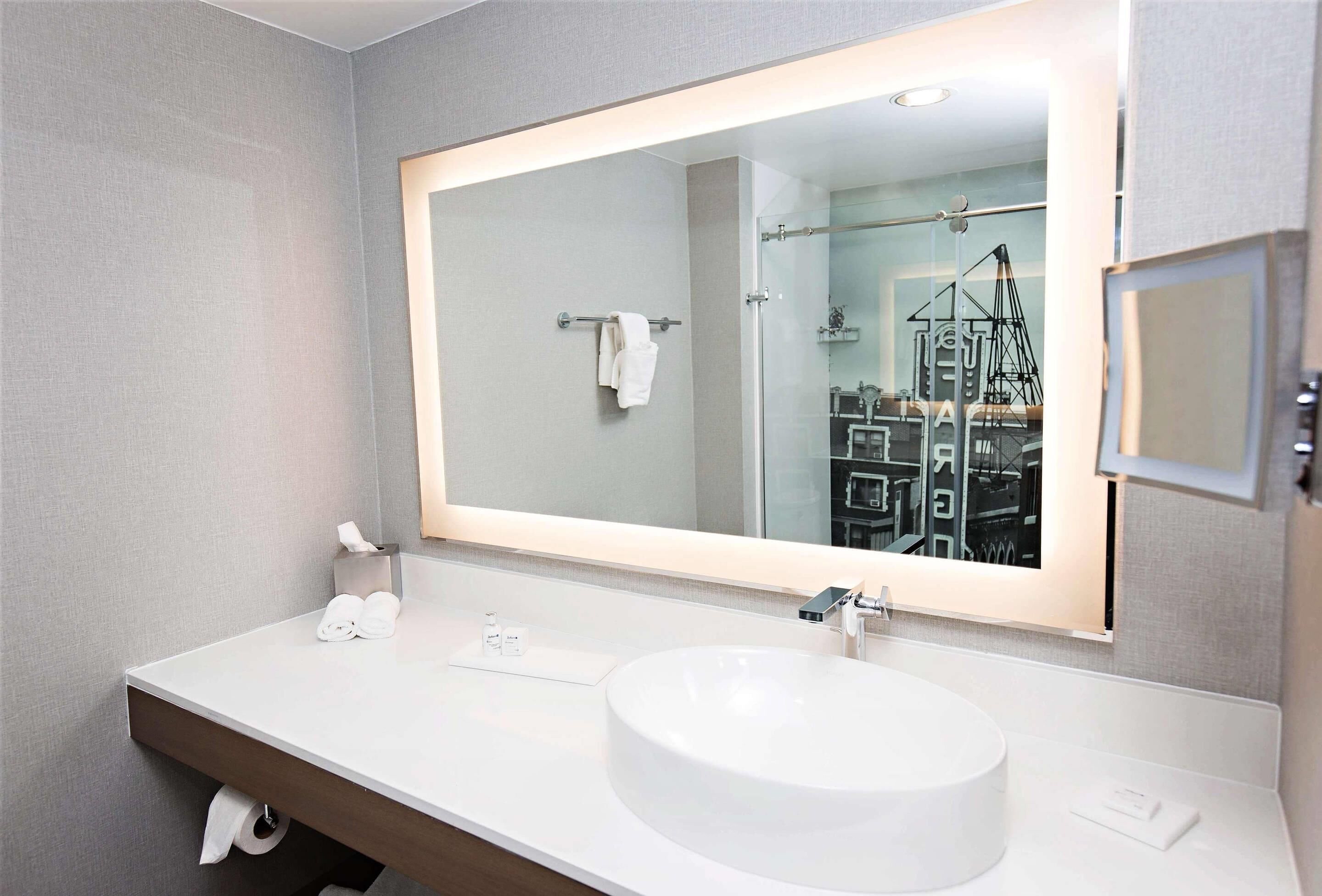 Une salle de bain moderne avec un grand miroir, un lavabo rond et un porte-serviettes.