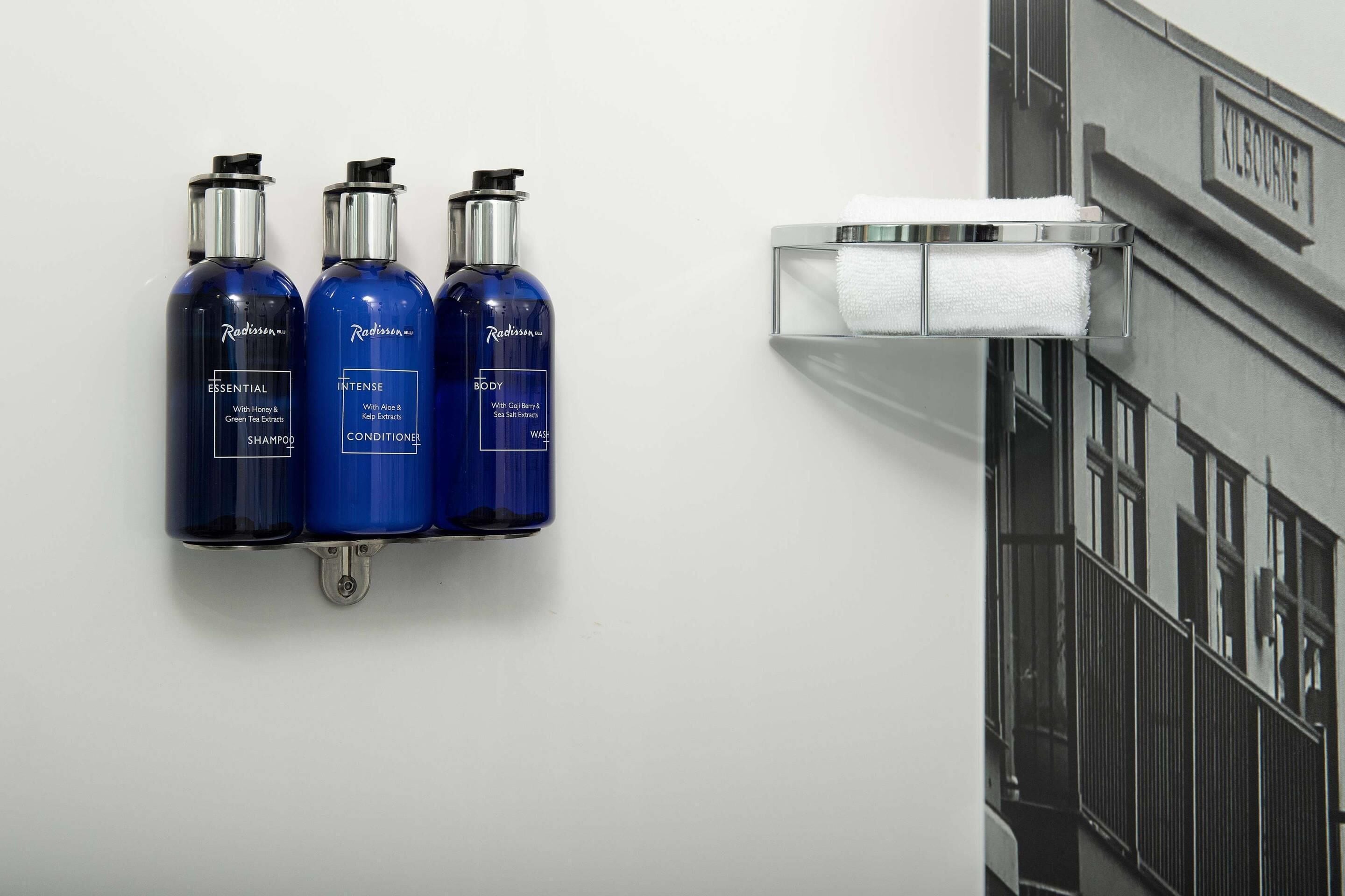 Een badkamer met drie verzorgingsproducten van Radisson op een wandplank.