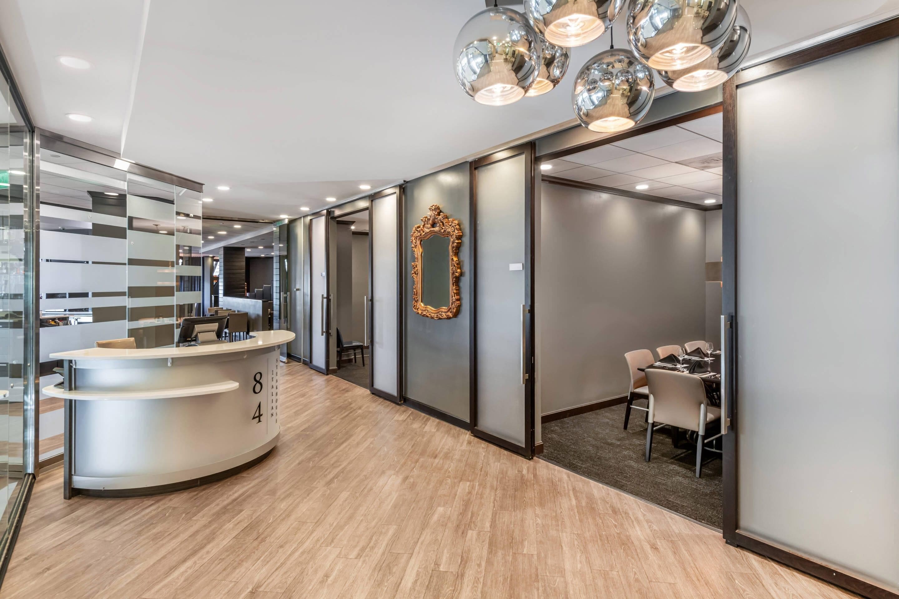 A modern hotel lobby with a reception desk, a mirror, and a dining area.