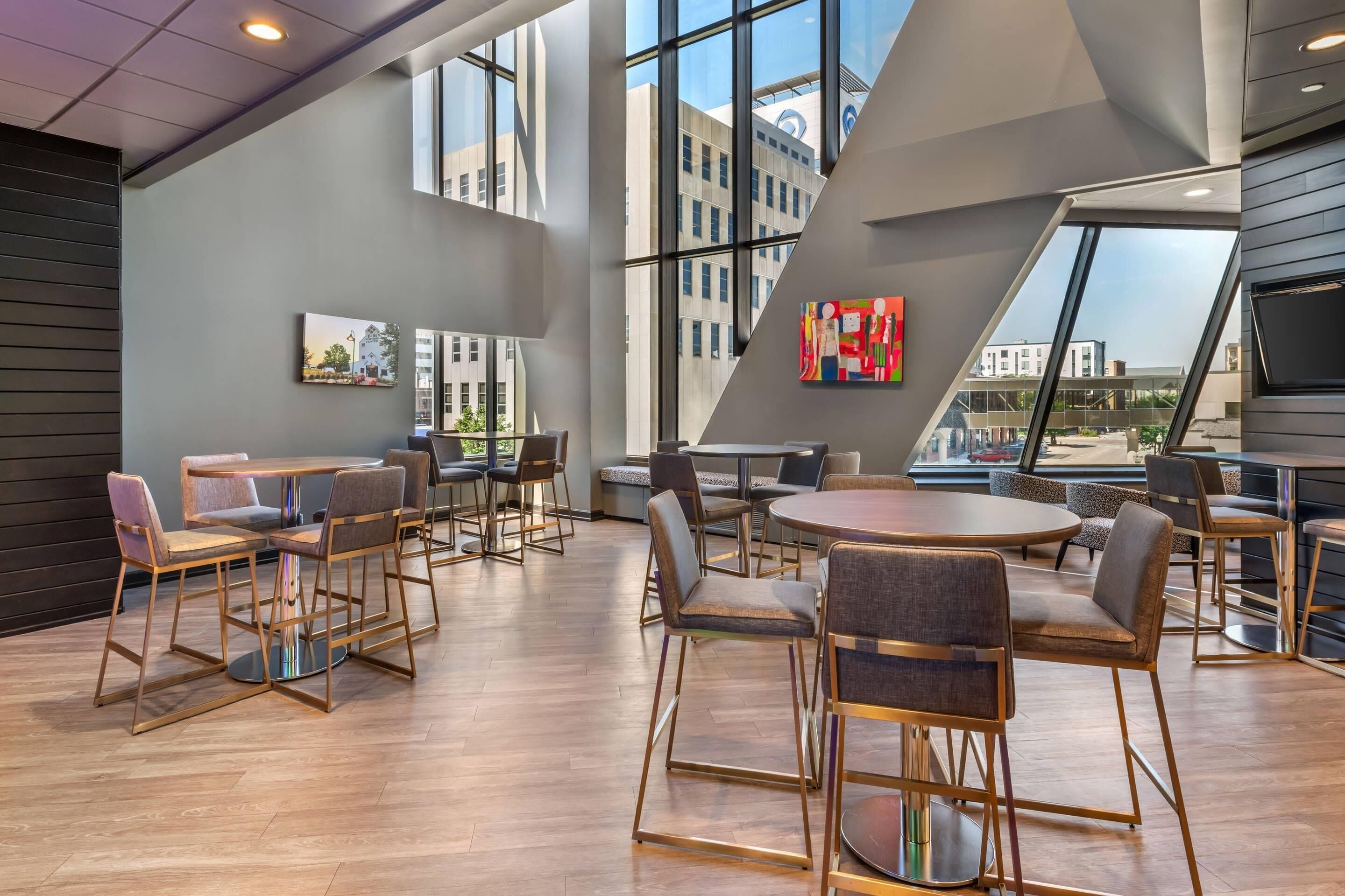 A modern interior with high ceilings, large windows, and a mix of seating arrangements including tables and chairs.