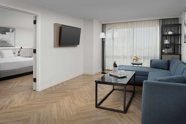 Quarto de hotel moderno com cama, televisão, sofá, mesa de centro e estante de livros.