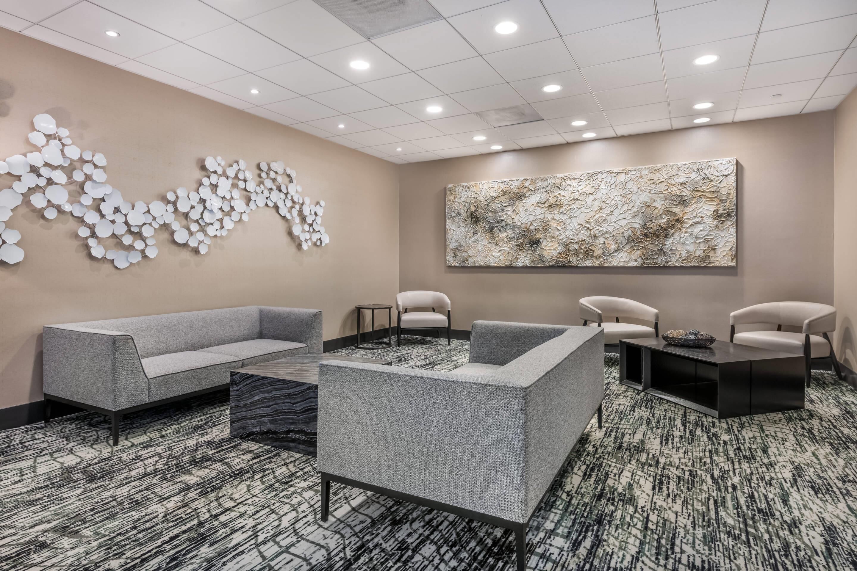 A modern lounge area with a grey sofa, armchairs, a coffee table, and a large abstract painting on the wall.