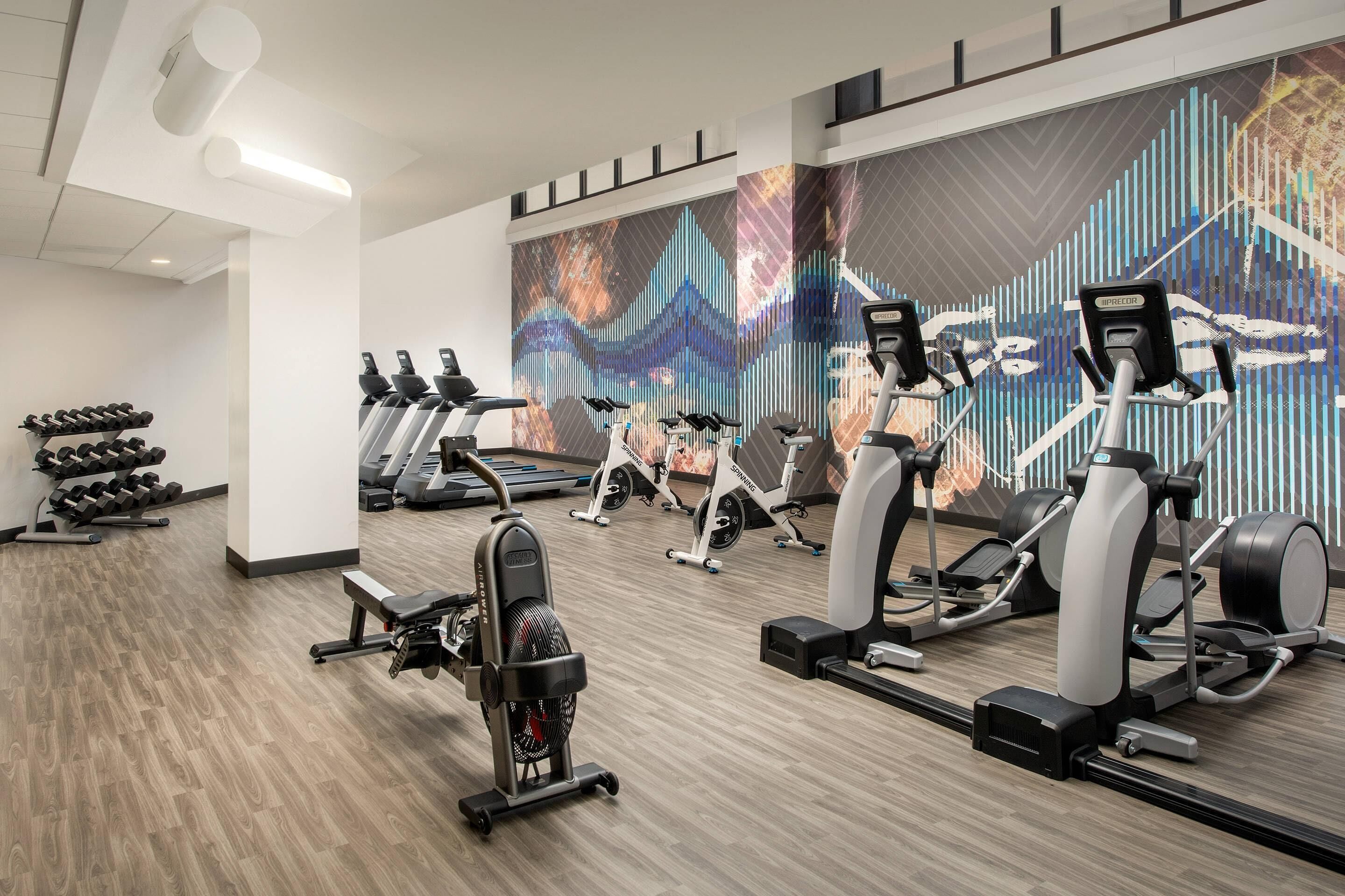 Un gimnasio con cintas de correr, bicicletas estáticas y una máquina de remo.