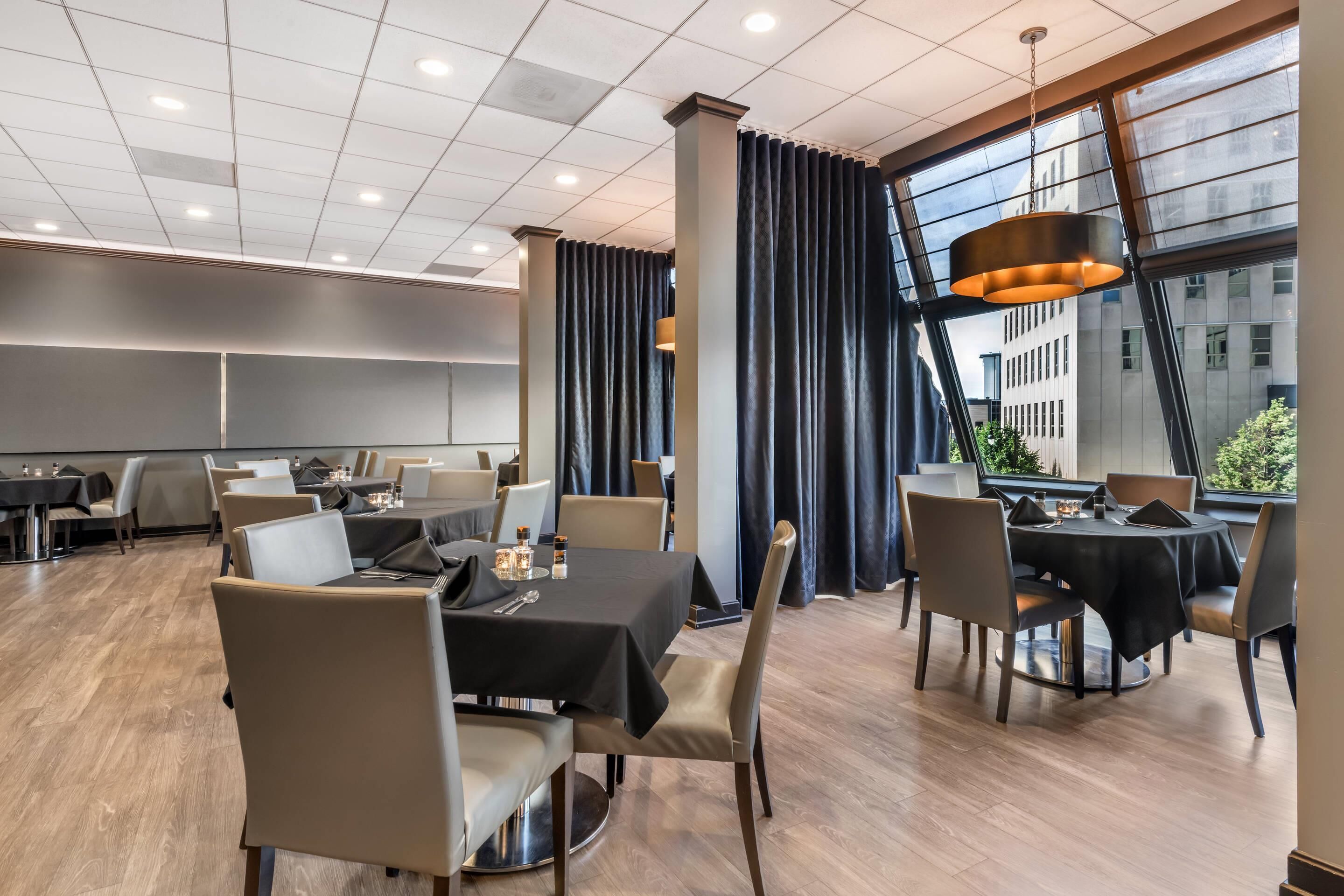 A modern dining area with tables and chairs, large windows, and a view of the city.